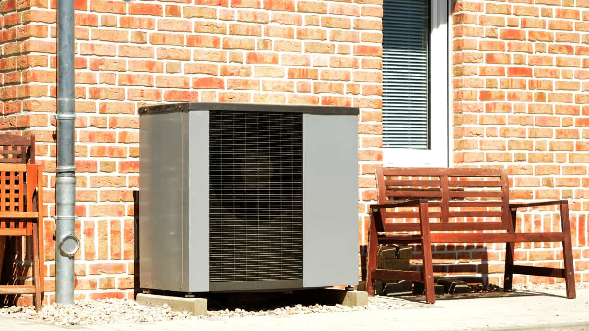 Buitenunit van een lucht-water warmtepomp tegen een bakstenen gevel van een woning.